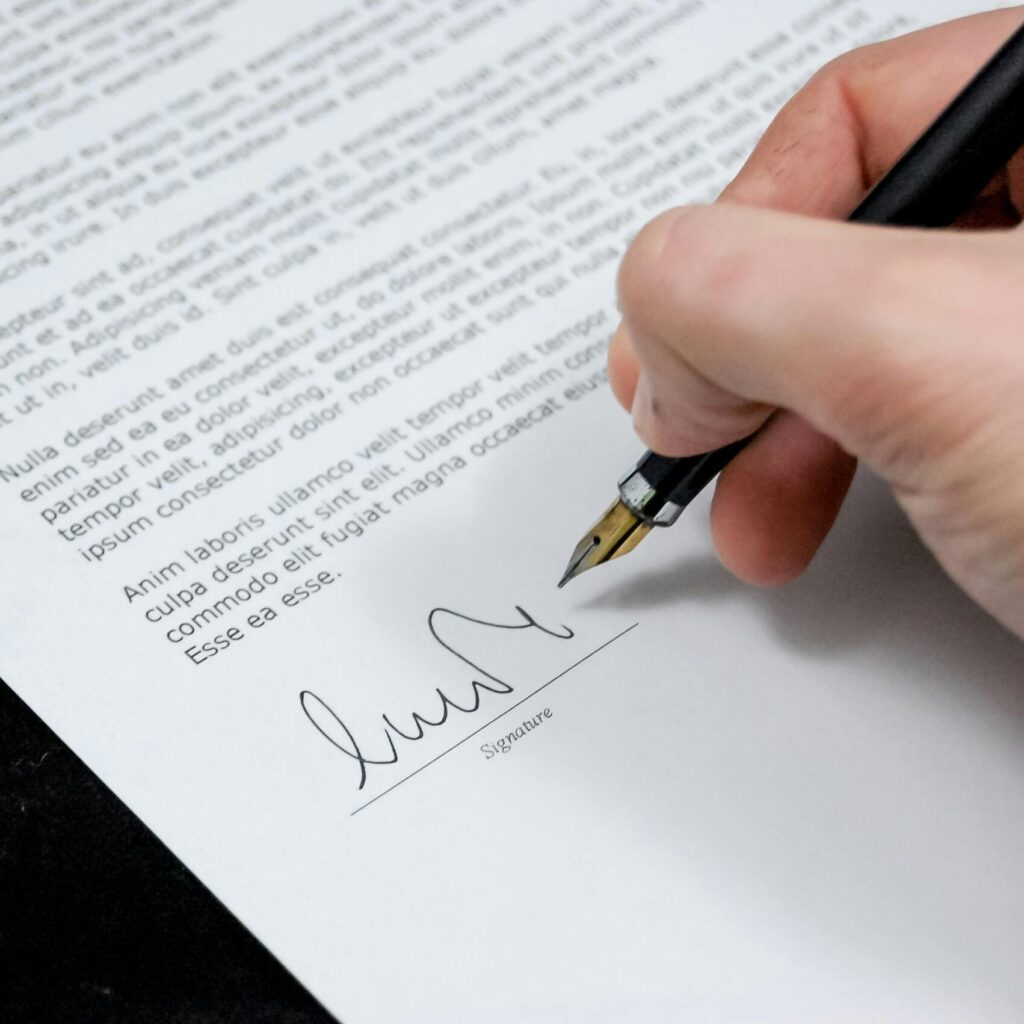 Close-up of a hand signing a formal document with a fountain pen, indicating agreement.
