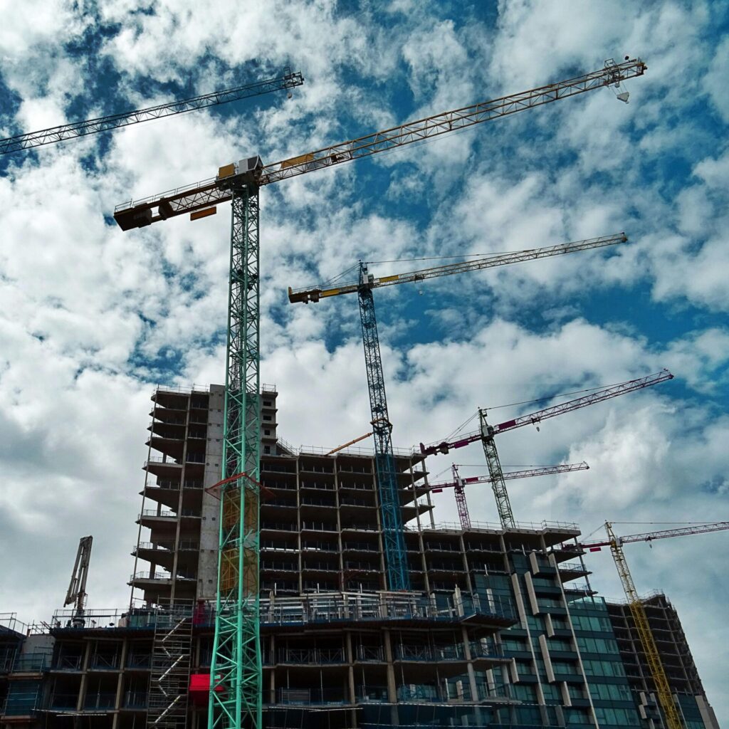 Urban construction site with numerous cranes framing rising skyscrapers against a blue sky.