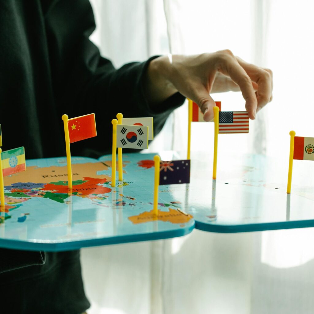 Hand arranging flags on a world map, signifying global diversity.